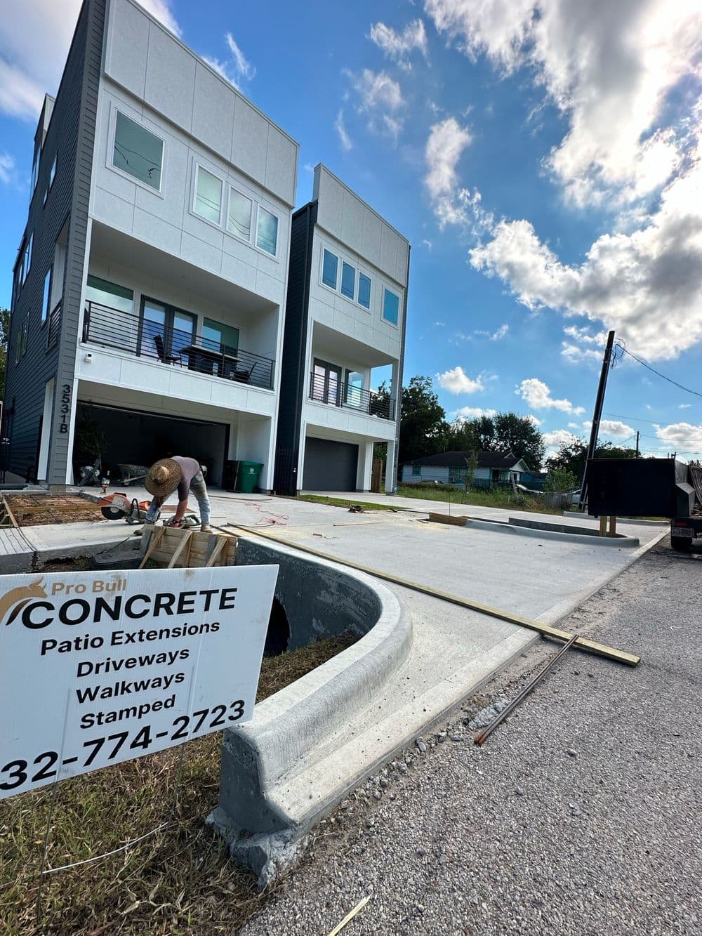 Concrete patio extension being installed near modern multi-story buildings. Pro Build Concrete sign visible.